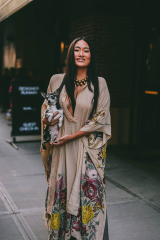 woman with beige dress with flower details, holding a small dog