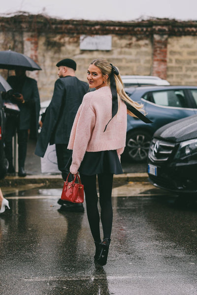 woman with pink cardigan, black shorts and tights and hair tied with a black bow