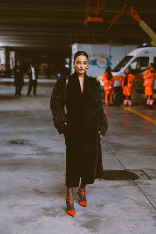 woman wearing a dark brown coat with textured sleeves, black tights and red heels