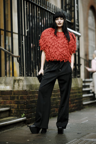 woman with black trousers, high heeled platform black shoes and red textured blouse
