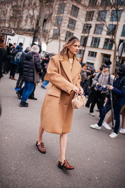 woman with headband, camel coat and brown leather brogues