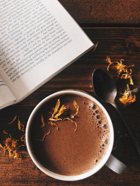 a cacao mushroom elixir in a coffee cup topped with calendula petals