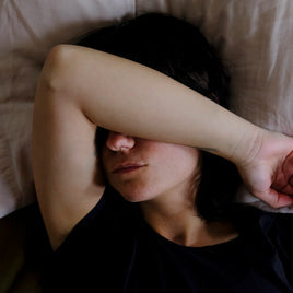Femme en train de dormir dans son lit, la tête sur son oreiller avec un bras sur le visage pour se cacher de la lumière