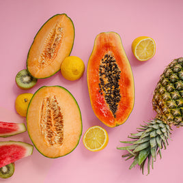 Différents fruits exotiques, ananas, papaye, éparpillés sur une table avec un fond rose