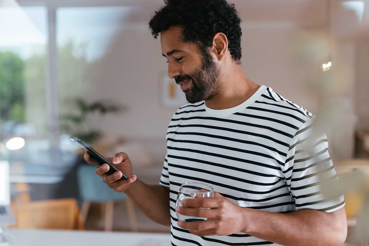 A light-skinned bearded man checking his phone while holding a glass of water.