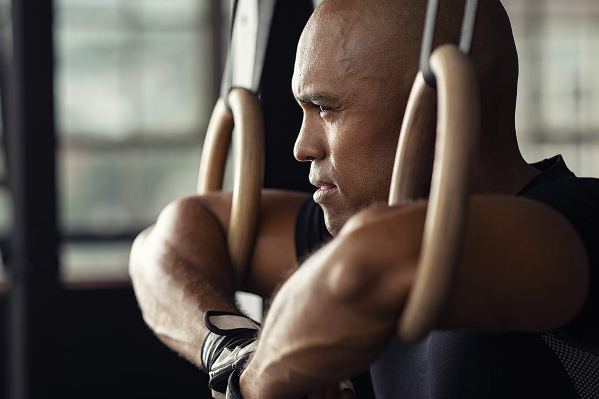 Dark-skinned man gazing forward with determination as he works out on rings.