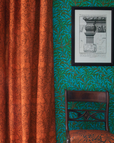 Zeleno-modrá vzorovaná tapeta a oranžový  záves značky Morris & Co