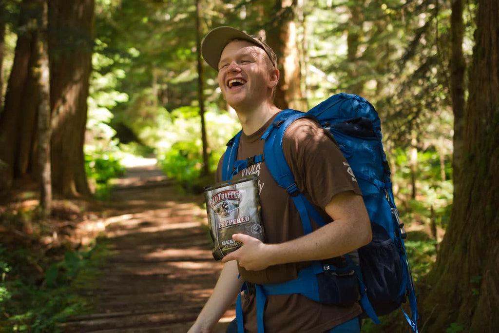 A hiker enjoying a bag of Old Trapper Peppered beef jerky while on the trail.