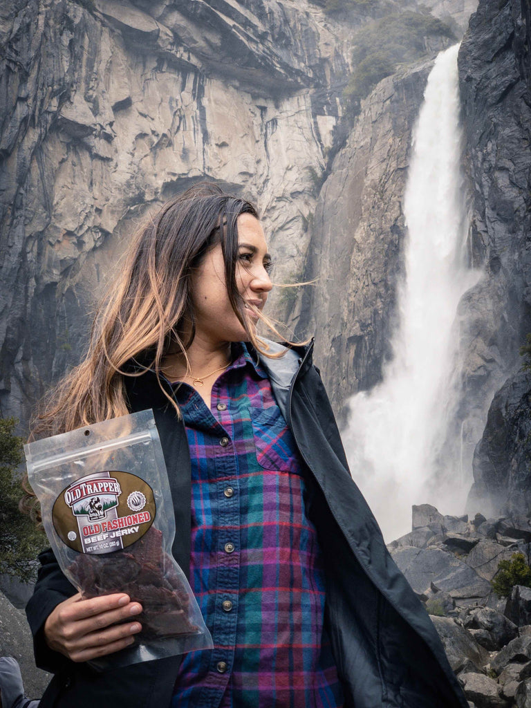 Woman holding a bag of 10oz Old fashioned beef jerky at the base of lower yosemite falls