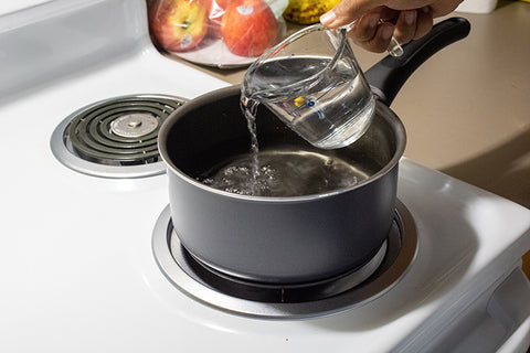 Pouring pouring water from a glass measuring cup into a pot on a stove