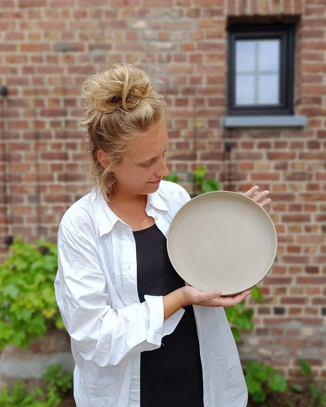 Andrea admires a freshly crafted ceramic plate in her studio