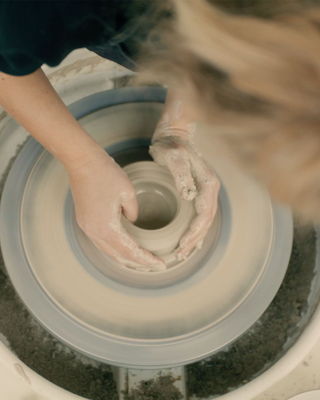 Andrea’s hands masterfully shaping a clay pot on a spinning wheel.