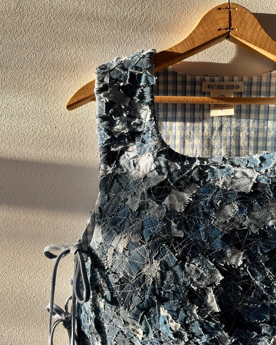 Hailey's handcrafted denim garment hangs on a wooden hanger, illuminated by natural light that highlights the textured patchwork and detailed stitches, reflecting the creativity in women's fashion design.