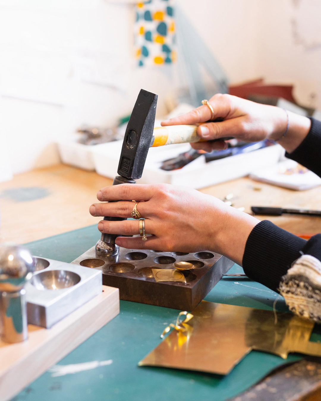 artisan shaping jewelry with a hammer in her workshop, an image of her craft and precision.