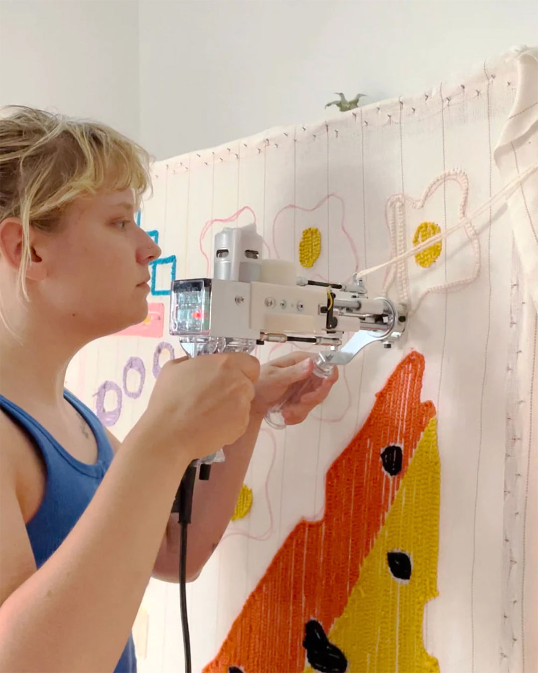 Angela uses a tufting gun to weave a bold pattern into fabric, demonstrating women creativity in textile design.