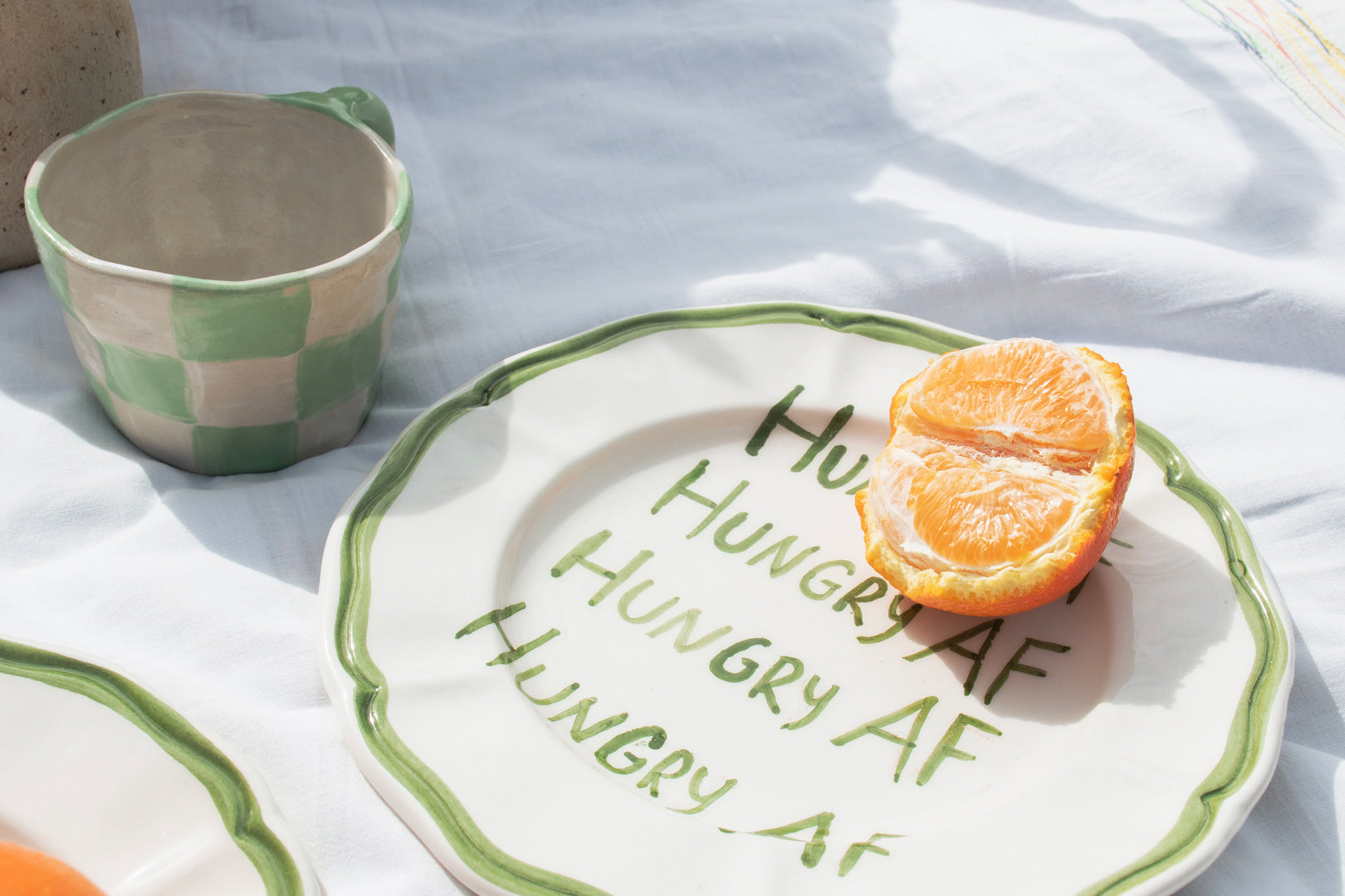 An up-close view of ceramic picnicware, featuring a green-striped bowl with a juicy orange slice, on a white linen background.