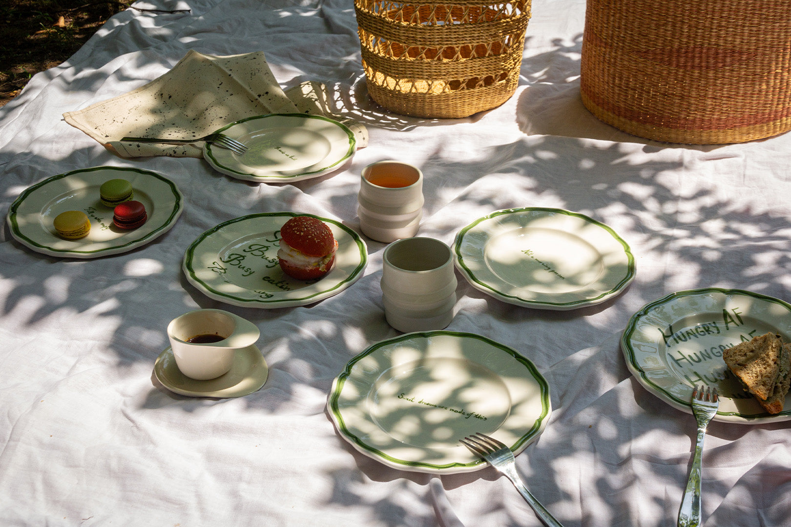 A complete eco-friendly picnic spread featuring ceramic plates with playful inscriptions, surrounded by a natural basket and cloth.A complete eco-friendly picnic spread featuring ceramic plates with playful inscriptions, surrounded by a natural basket and cloth.