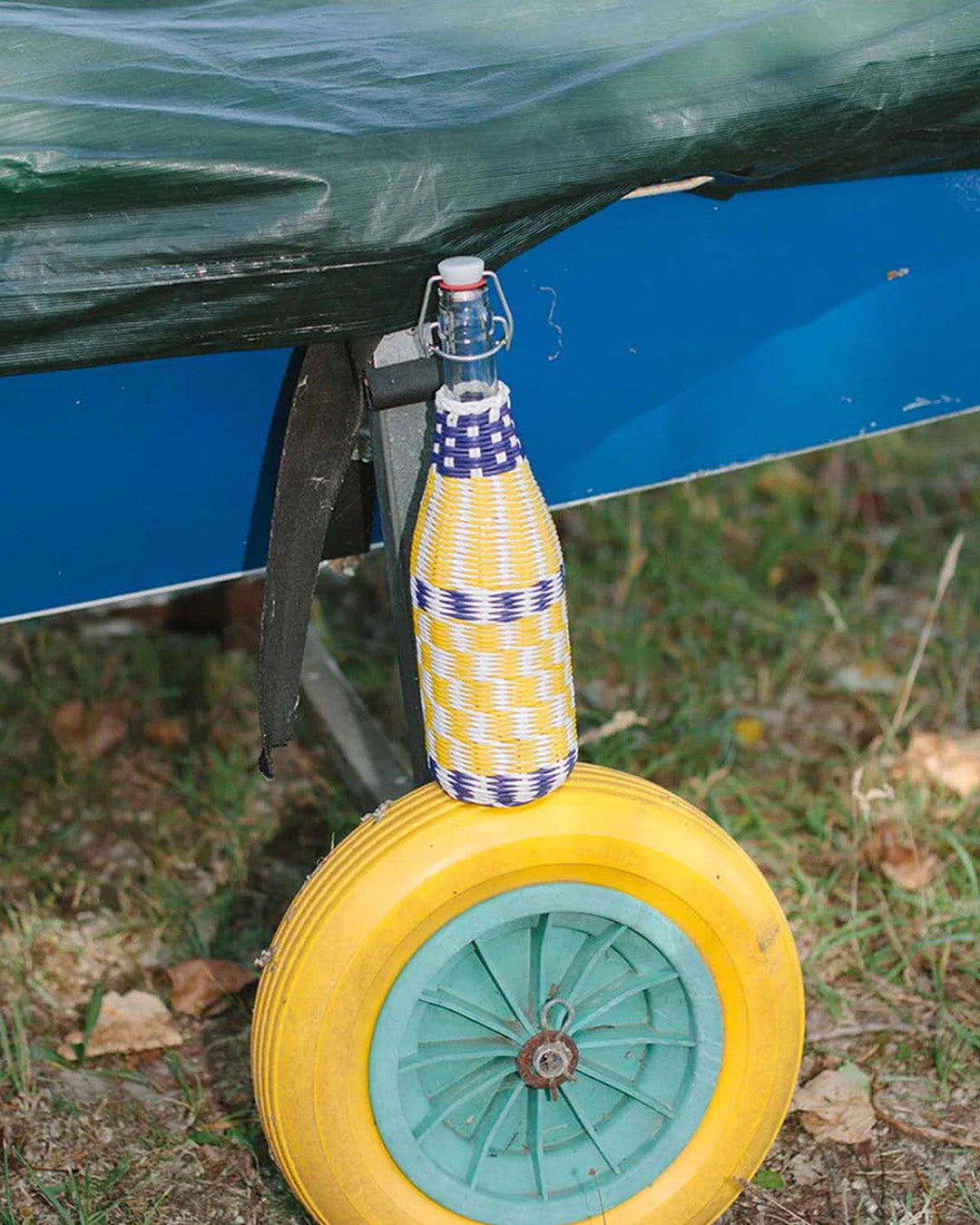 A colorful, handwoven bottle wrap with recycled plastic secured to a yellow wheel.