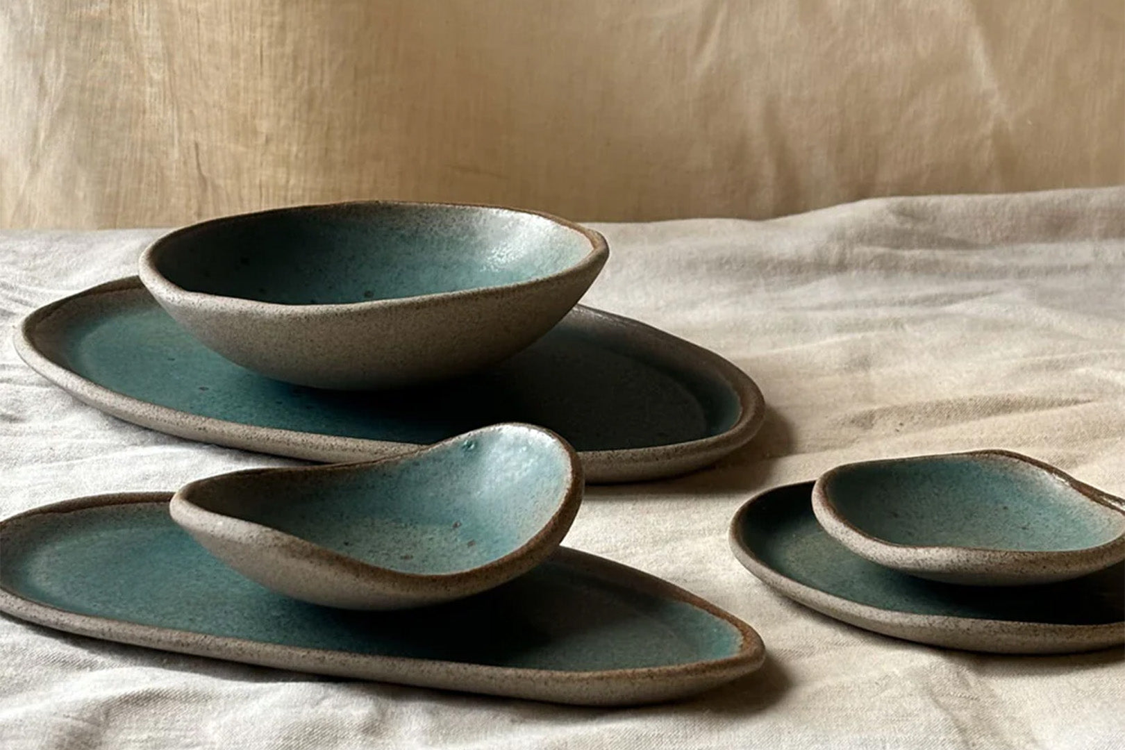 Artisanal ceramic dishware with a unique teal glaze, arranged thoughtfully on a neutral textile.