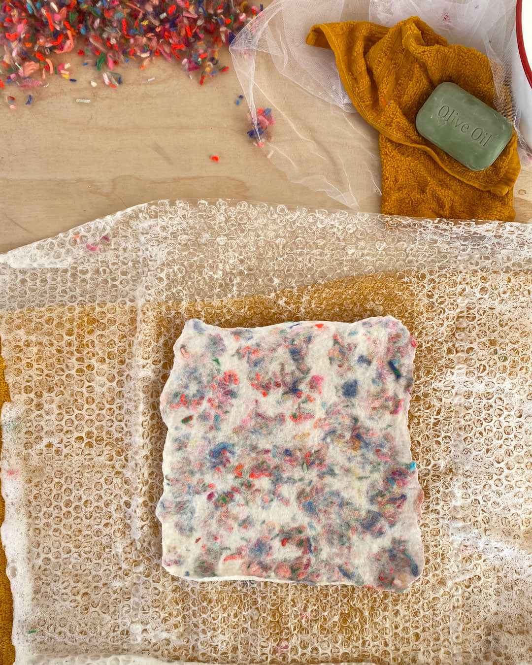 op view of a wet felting workspace with a bubbled wrap, showcasing the end of a beautiful wool felt piece with mixed scraps.