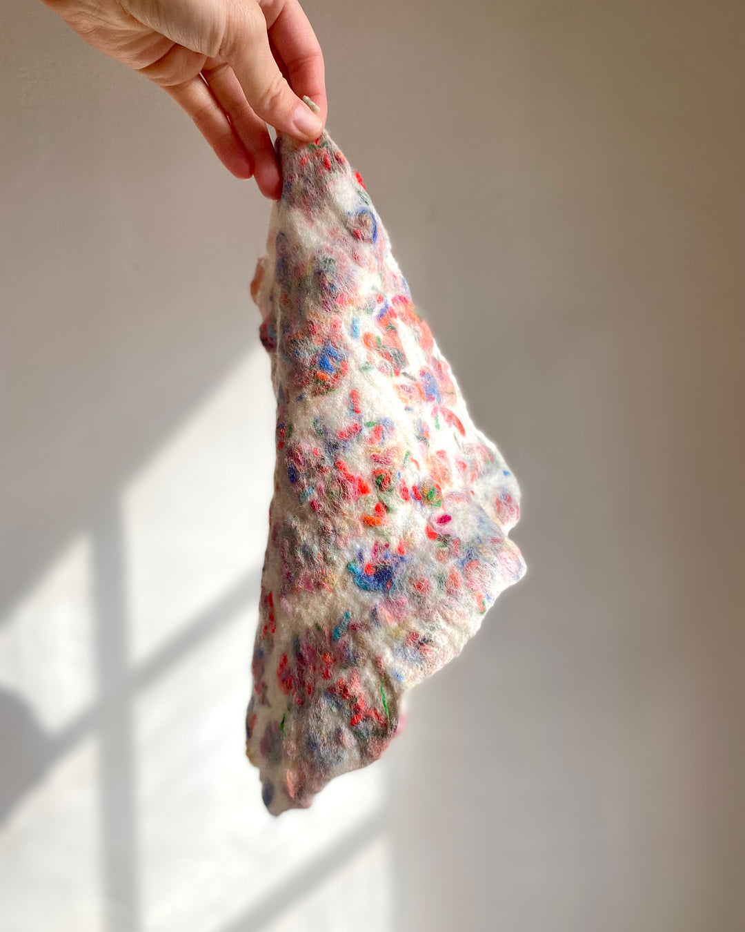 A hand-held piece of freshly wet-felted fabric with vibrant wool scraps, against the soft light creating a dreamy texture.