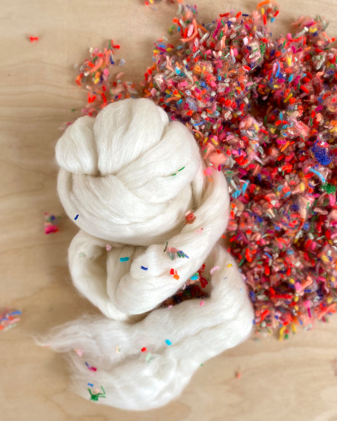 Close-up of white wool roving with flecks of colorful felting pieces, capturing the texture and detail of materials.