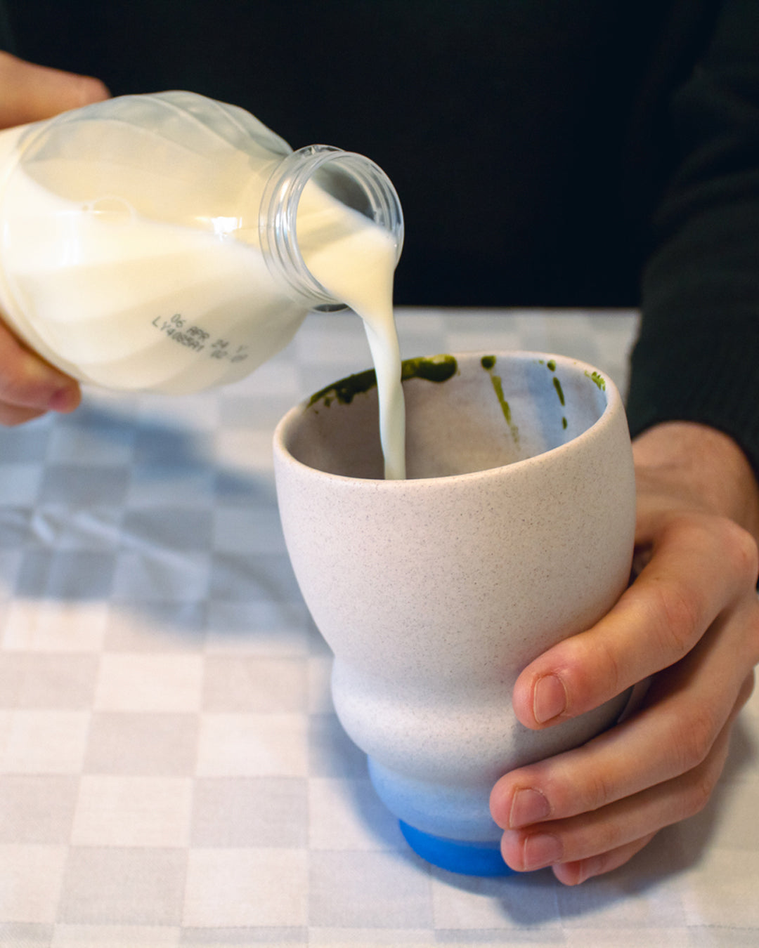 Pouring milk into a cup of matcha, a key step in the matcha latte-making process.