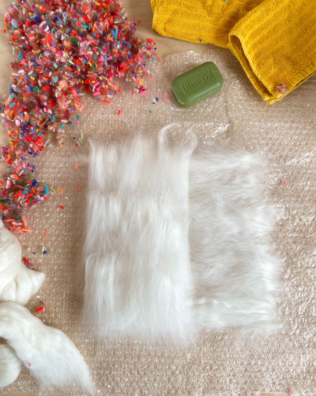 A tidy workstation with pure white wool roving and colorful wool snippets ready for a wet felting session.