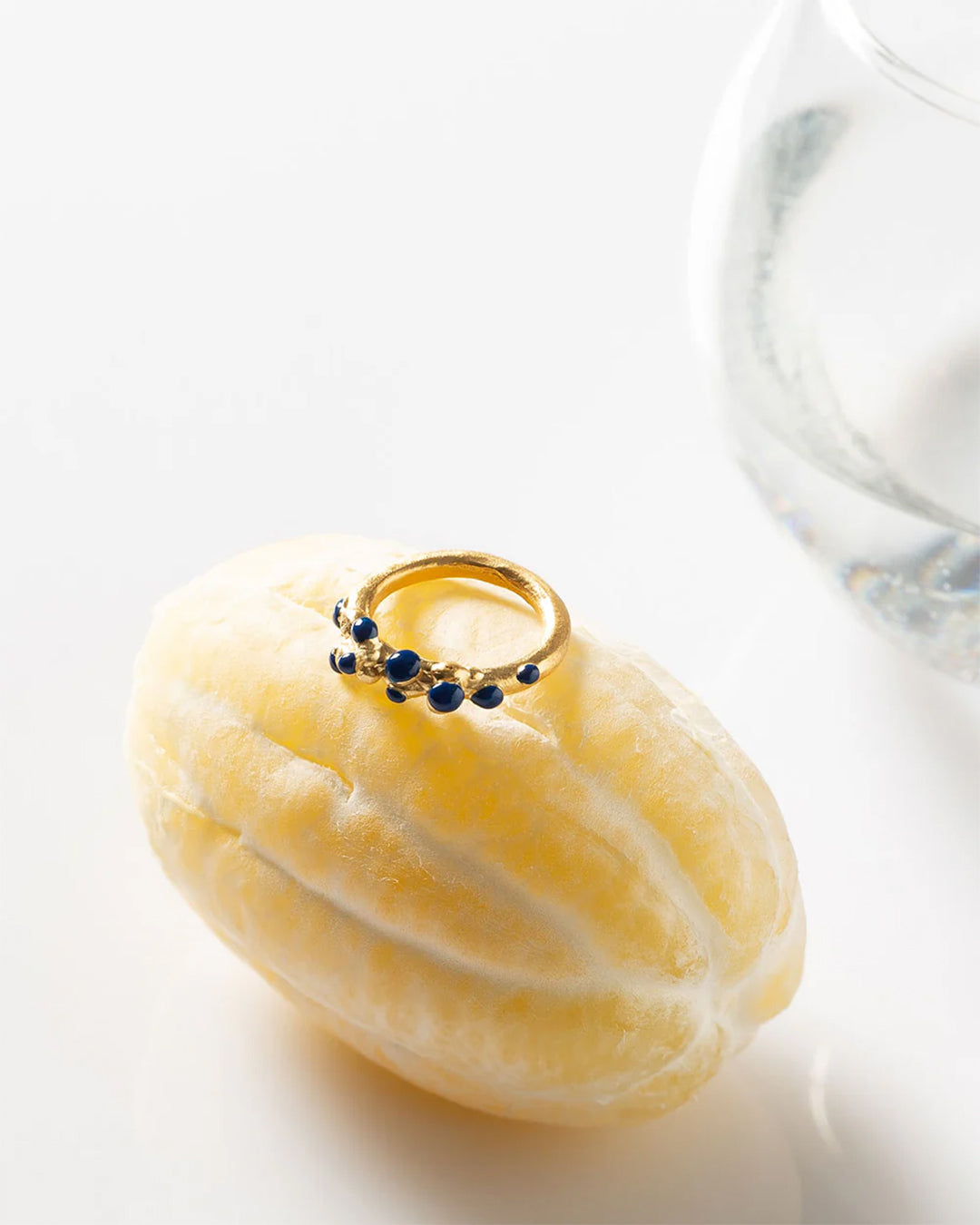 Elegant gold ring with blue stones presented on a lemon, crafted by artisan, symbolizing fresh, innovative design.