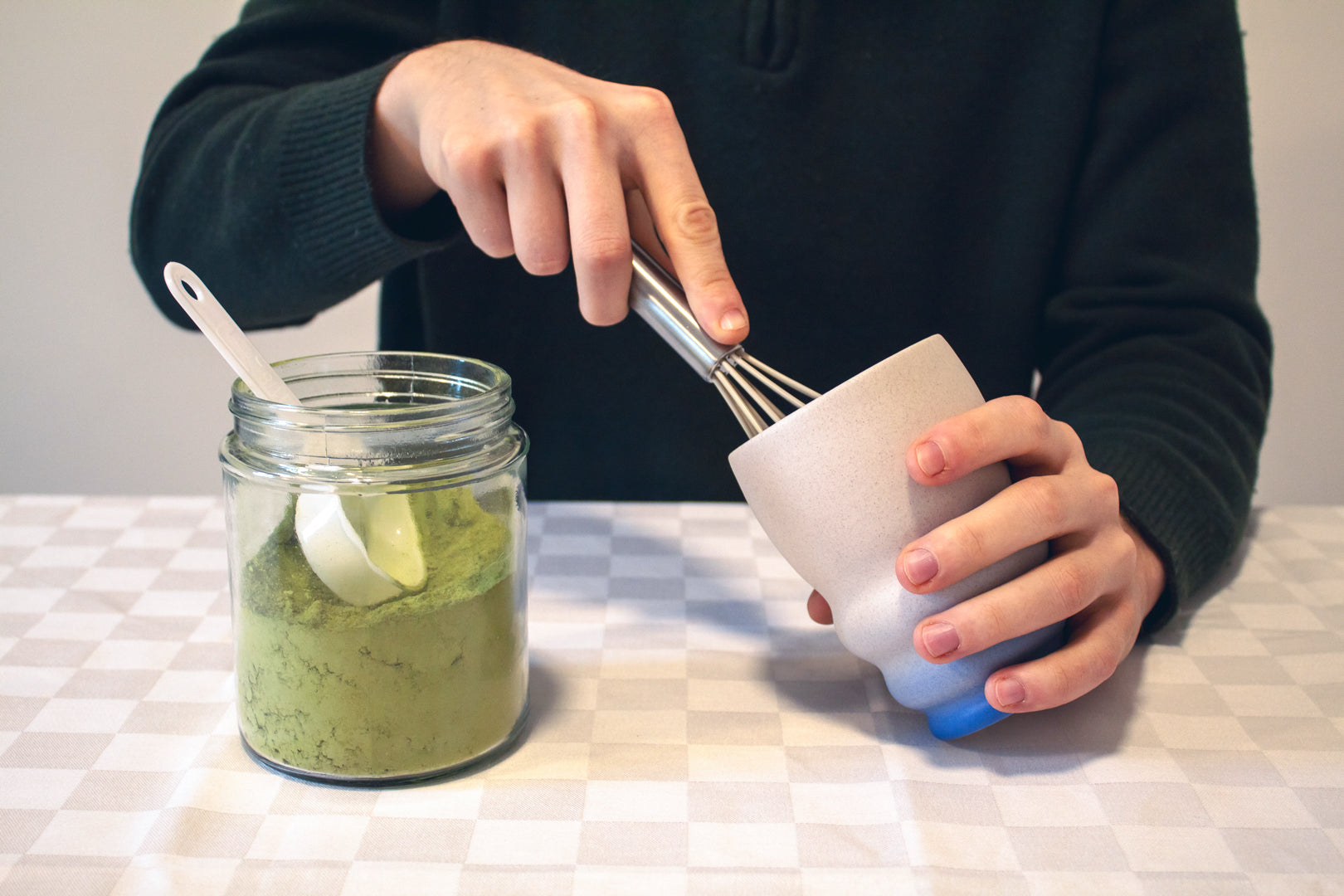 Hands holding a cup, demonstrating the whisking step in a matcha latte preparation guide.