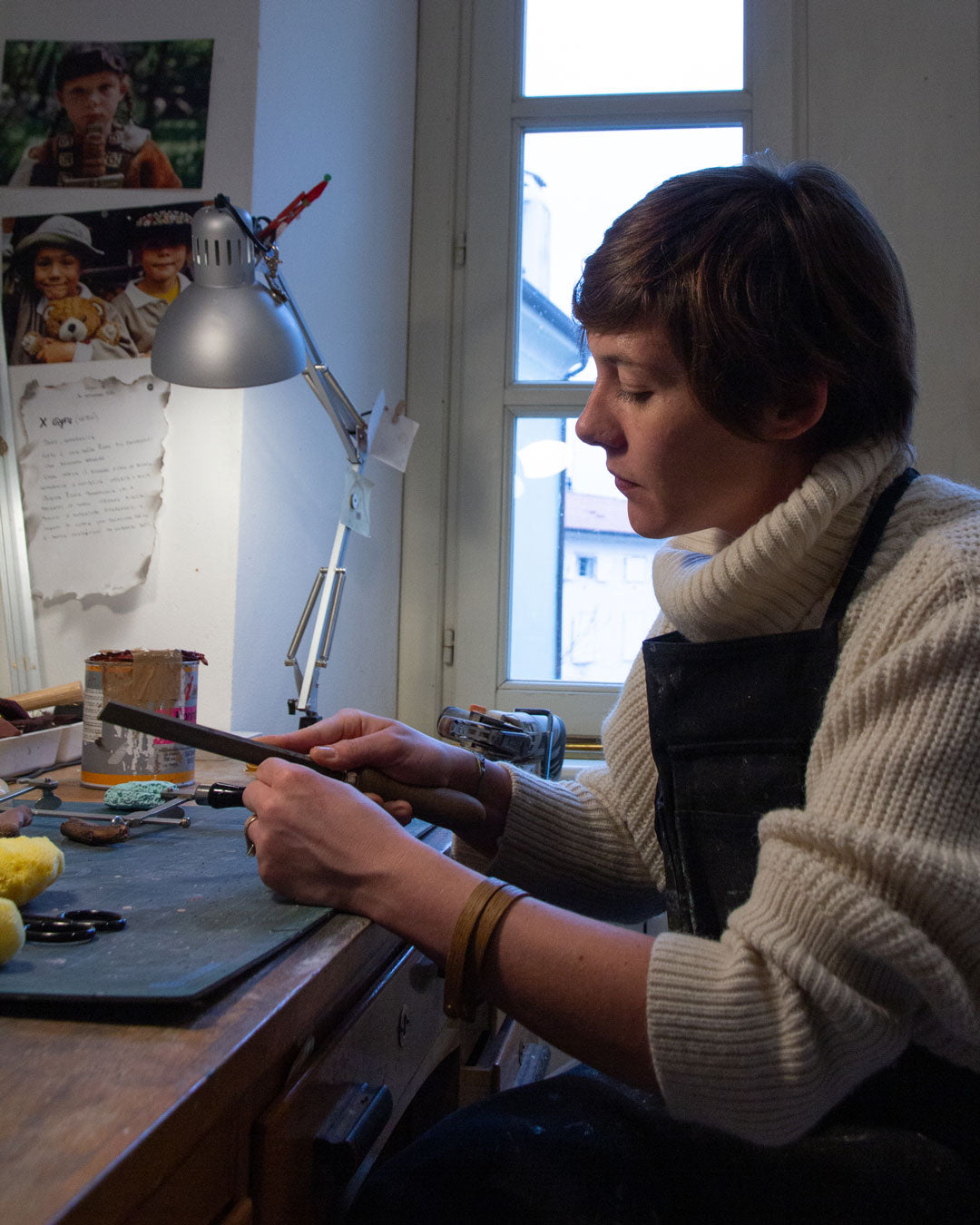Creative mom working on jewelry pieces in her well-lit workshop surrounded by tools and her craft's inspirations