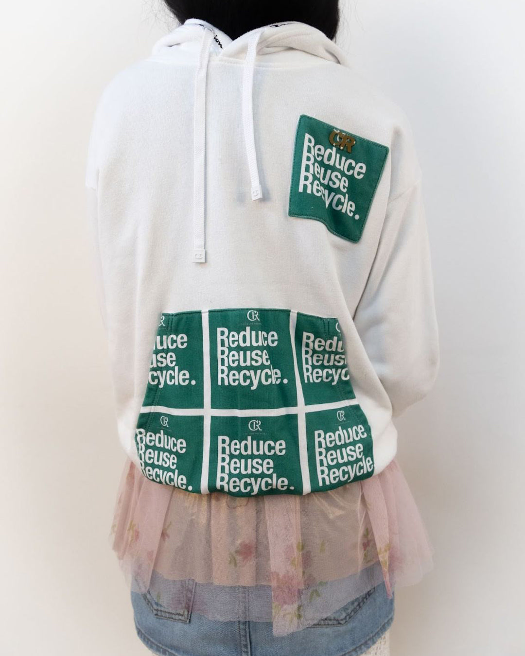 Rear view of a person wearing a white hoodie with 'Reduce, Reuse, Recycle' patches, embodying the sustainable movement's principles in their attire.