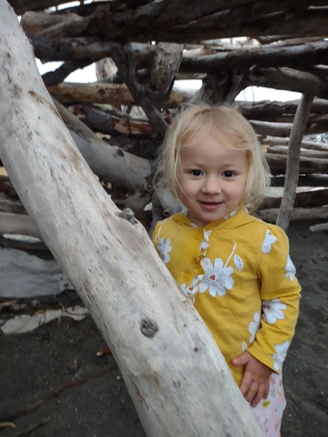 A two year old smiles in a Driftwood structure at Moonstone Beach in Cambria