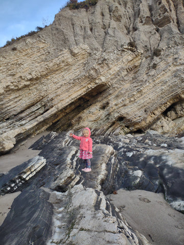 A little girl dressed in pink, gestures to the access point to tidepools in Pismo Beach with dramatic uplifted rock behind