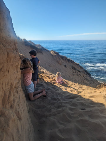 Kids play in a sand cliff as the waves crash while sitting on a large sand dune in montana de oro, san luis obispo county, california's central coast.