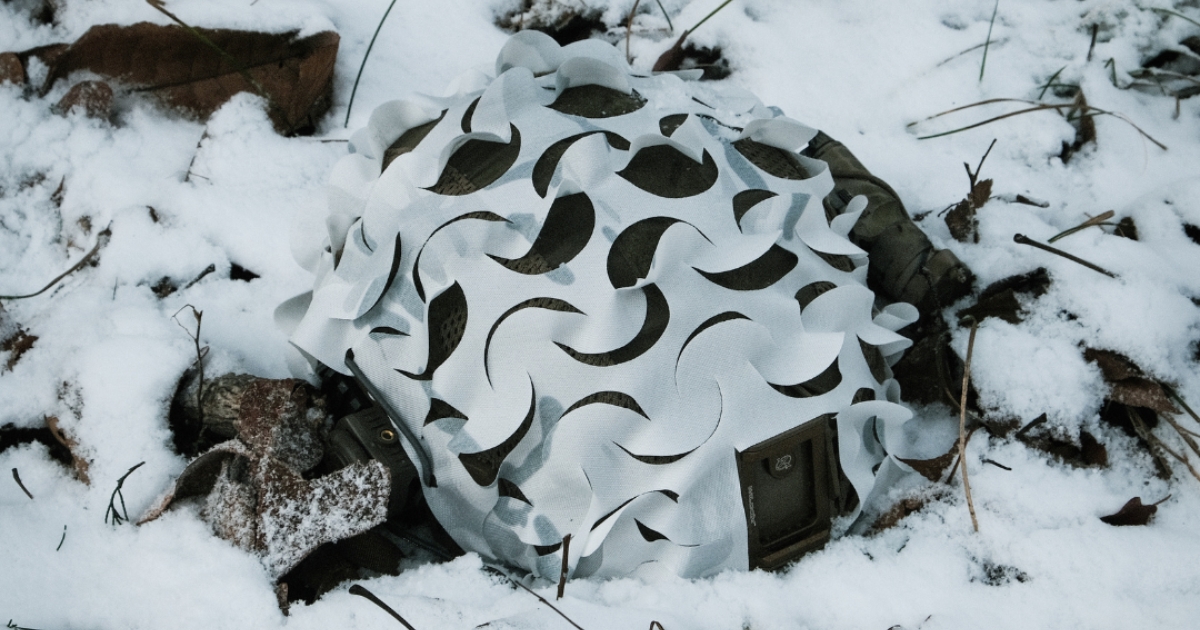 A helmet laying in the snow covered with a white helmet scrim.