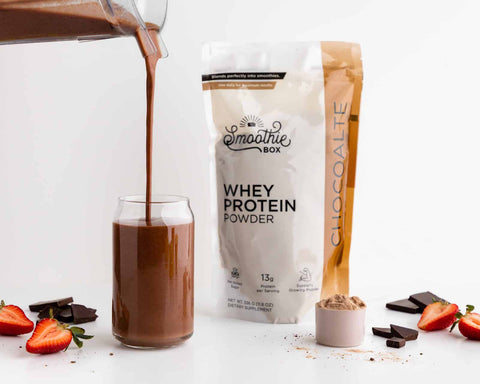 chocolate smoothie being poured into a glass along side chocolate protein powder