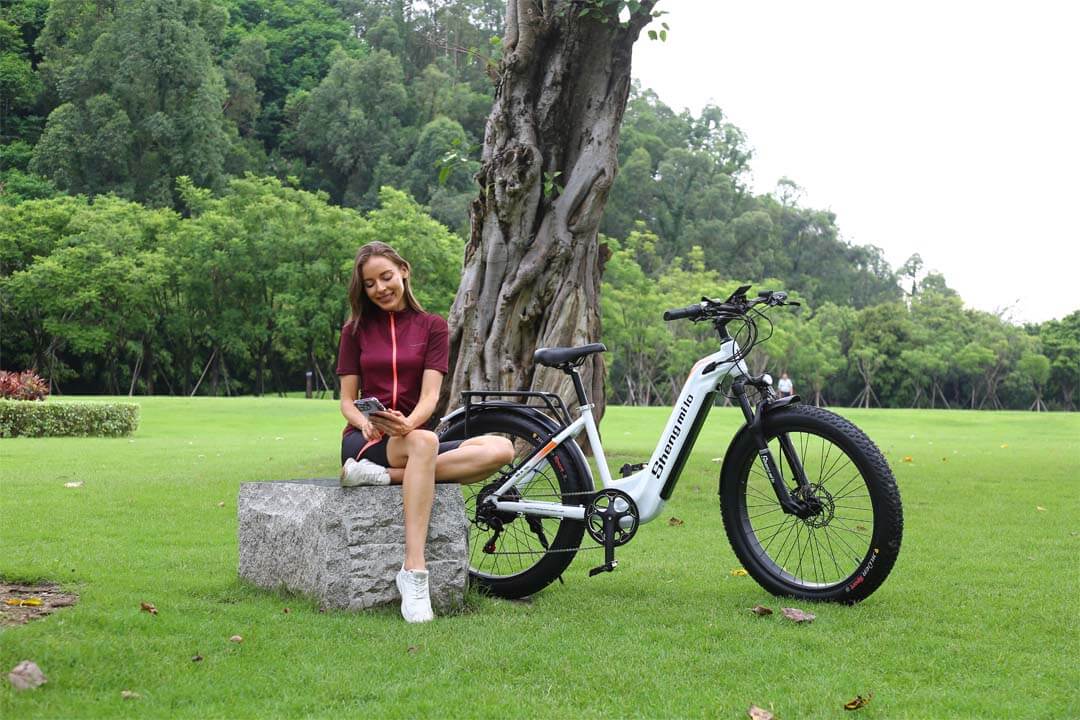 Femme se reposant sur un banc en pierre près d'un vélo électrique garé.