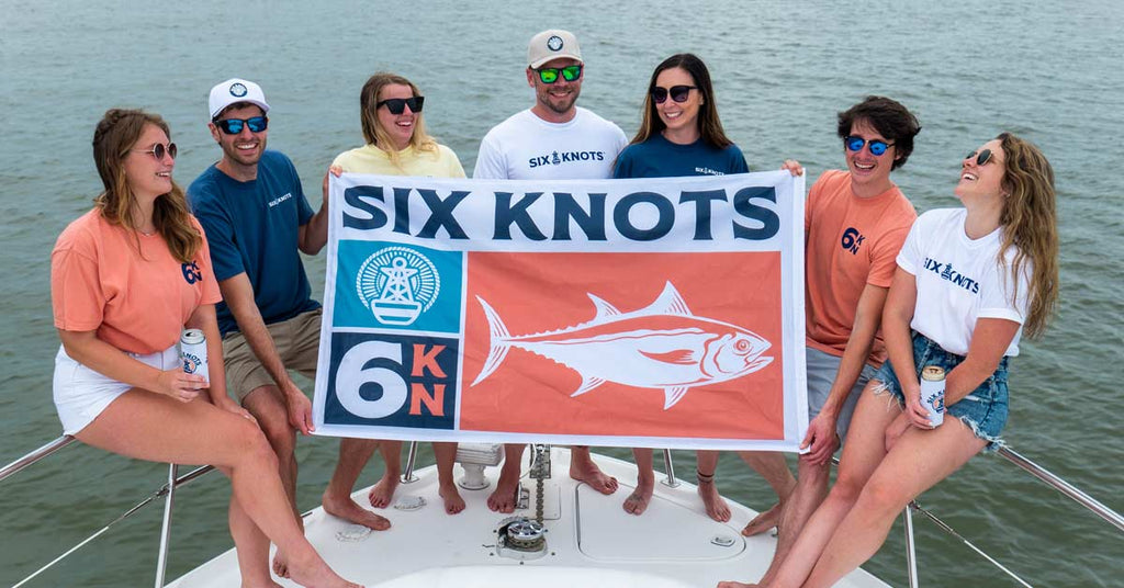 Group of people on a boat holding a Six Knots flag