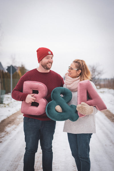 Pareja enamorada sosteniendo cojín de letras B y A antes de fiesta baby shower