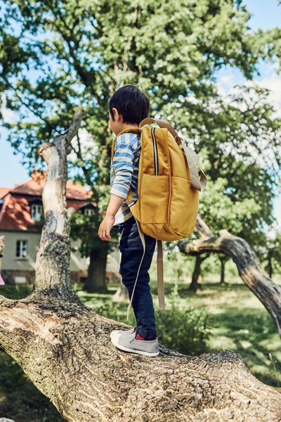Ein Junge spielt nach der Schule auf einem Baum mit einem samtgelben Rucksack. kleiner Rucksack für den Kindergarten