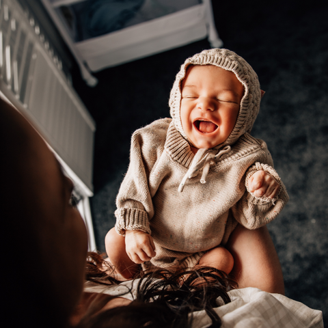 image of baby smiling and laughing in mothers arms near a window