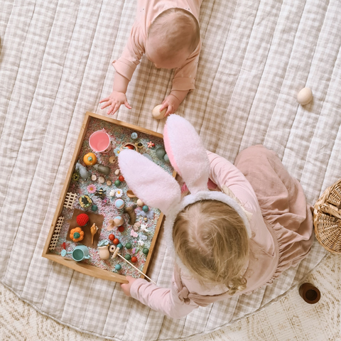 Baby and toddler on a waterproof playmat playing with an Easter sensory tray