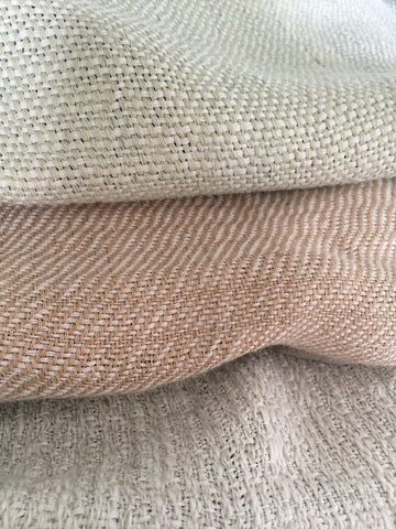 Three hand-woven textiles, stacked on top of each other in pastel spring hues
