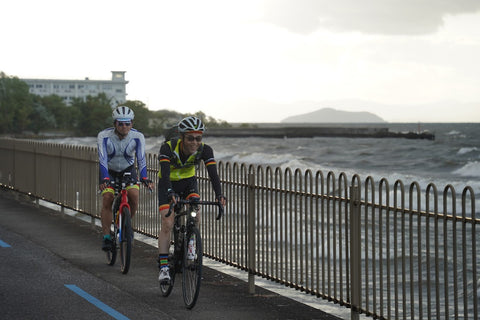 琵琶湖の湖畔を自転車で走る2人を正面から撮影