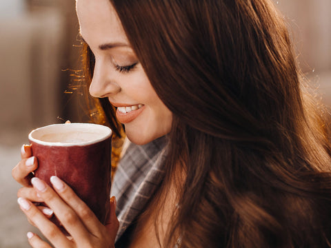 A young woman smiles lovingly over a warm cup of coffee.