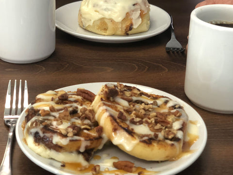  Two people sitting at a table ready to enjoy cinnamon rolls and delicious hot coffee.