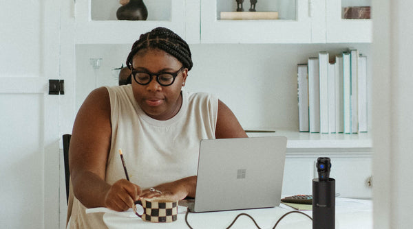 female small business owner writing with a pencil in front of laptop and the Toucan Video Conference System 360 on the white round table