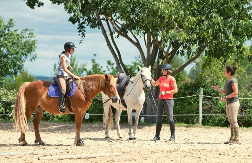 Two girls learning how to ride a horse from a female instructor