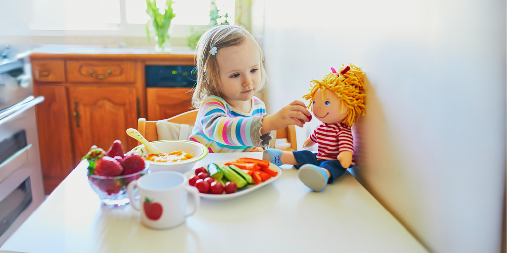 toddler eating vegetables and playing with doll